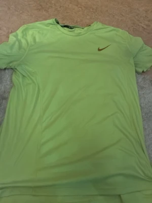 Nike Dri-Fit limegrön t-shirt - Limegrön t-shirt från Nike med Dri-Fit material som håller dig torr under träningen. Perfekt för löpning och andra sporter, med diskret Nike-logga på bröstet och rund hals. Materialet är lätt och andas bra.