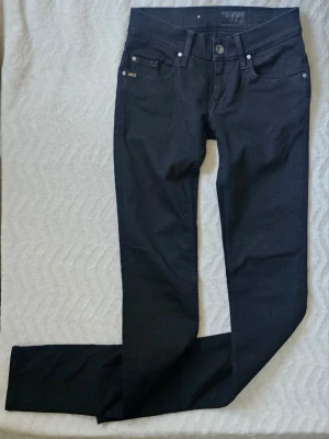 Svarta jeans från Tiger of Sweden - Snygga svarta jeans från Tiger of Sweden med klassisk femficksmodell och raka ben. Jeansen har silverfärgade nitar och en liten logotypetikett vid fickan. Materialet är mjukt och stretchigt för extra komfort.