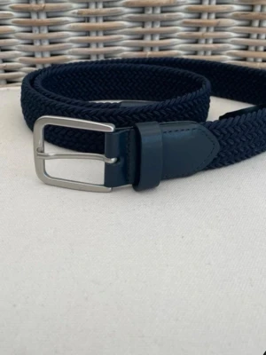 Mörkblå flätat bälte med silverfärgat spänne - Snyggt mörkblått flätat bälte med silverfärgat metallspänne och detaljer i skinn. Perfekt för att ge din outfit en stilren touch. Bältet har en klassisk design med flätad struktur och är lätt att justera.