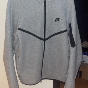 Grå hoodie från Nike med dragkedja - Säljer min Nike tech pågrund av stor viktnedgång, fick den av en släkting på födelsedagen kunde inte returnera den för att var iväg i 4 veckor. Den är använd 5ggr om inte mindre tvättad två, materialet är fortfarande lent som den vore sprillans ny. (Kan komma överens om ett bra pris)😁😁
