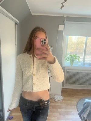 Vit croppad kofta med knappar från h&m - Säljer en fluffig vit croppad kofta med stora dekorativa knappar i guld framtill. Koftan har lång ärm och är gjord i ett mjukt, stickat material som ger en mysig look. Perfekt att styla med jeans för en trendig outfit. Använd fåtal gånger💓💓