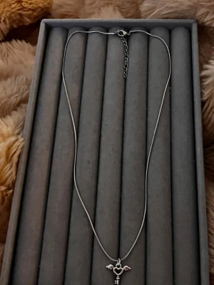 Silverhalsband med hjärtnyckel och vingar - Snyggt silverfärgat halsband med ett hängsmycke i form av en nyckel med hjärta och små vingar på sidorna. Kedjan är tunn och smidig, och smycket har en unik och lekfull design. Perfekt för dig som gillar detaljerade accessoarer med lite edge.