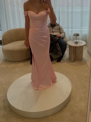 Ljusrosa balklänning med slits - Elegant ljusrosa långklänning med figurnära passform och hög slits på sidan, köpt på dressroom butiken i Göteborg. Klänningen har breda axelband, v-ringad urringning och fina draperingar över byst och midja. Perfekt för bal eller student. Klänningen har bara använts en gång, men kan vara i behov av kemtvätt. Den är i storlek 4 och är varken omsydd eller uppsydd så den sitter precis som den gör i butik. Jag är 175 cm lång 