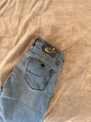 Blå jeans från Jacob Cohen model 622 comfort - Säljer ett par blå jeans från Jacob Cohen med klassisk femficksdesign och snygga detaljer. Jeansen har en mörkblå patch bak och guldfärgad dragkedja. Materialet är denim och modellen är rak. Perfekt för dig som gillar stilrena och exklusiva jeans.