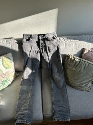 Grå raka jeans från Nudie jeans  - Säljer ett par grå jeans med klassisk femficksdesign och raka ben. Jeansen har knapp- och dragkedjegylf samt tydliga sömmar. Materialet är denim och färgen är en cool grå nyans som passar till det mesta. Nudie jeans, snygga slitningar och bra använda. Skick 8-9/10