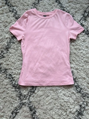 Ljusrosa t-shirt från SHEIN - En enkel och stilren ljusrosa t-shirt från SHEIN i storlek S. T-shirten har korta ärmar och rund halsringning, perfekt för att matcha med jeans eller kjol. Materialet är mjukt och känns bekvämt mot huden.