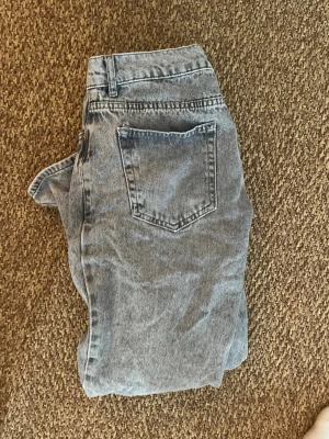 Grå tvättade  jeans - Säljer ett par grå mom jeans med tvättad look och raka ben. Jeansen har klassiska bakfickor och hög midja. Perfekta för en avslappnad och trendig stil. Materialet är denim i bomull.