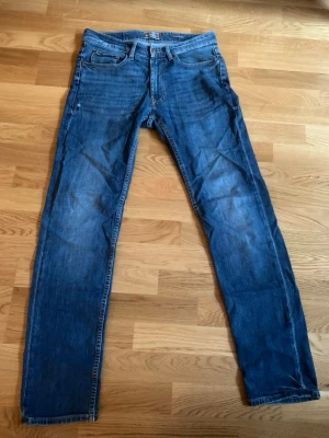 Dressman Mörkblå Jeans Regular Fit - Mörkblå jeans från Dressman i regular fit. Sparsamt använda med ett litet tecken på användning vid ena benet. Klassisk femficksmodell med koppardetaljer. Perfekta vardagsjeans!