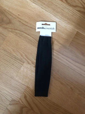 Svart hårband från needs.essentials - Säljer ett mjukt och stretchigt svart hårband från needs.essentials. Perfekt för att hålla håret på plats och ge en clean look. Helt ny i orginalförpackning.