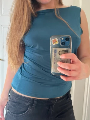 Blå ärmlös topp med bred halsringning - Snygg blå topp med bred halsringning som kan bäras offshoulder. Toppen är ärmlös och har en tight passform. 