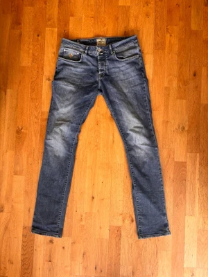 Blå Morris jeans me fades - Snygga blå Morris jeans med lätt slitna detaljer på framsidan och klassiska fickor både fram och bak. Jeansen har en modern passform och är tillverkade i denim med stretch för extra komfort. Perfekt för dig som gillar en avslappnad och trendig look. Jeansen är i storlek w31 l34