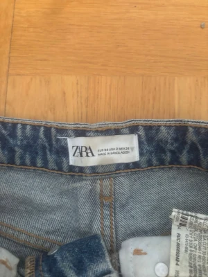 Blå jeansshorts från Zara - Säljer ett par klassiska blå jeansshorts från Zara i storlek 34. Shortsen har råa och fransiga kanter. De är högmidjade och gjorda i bomull för en skön och avslappnad look.