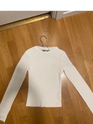 Vit långärmad topp från bikbok  - En enkel och stilren vit långärmad topp från bikbok. Modellen är slim fit med rund hals och är tillverkad i mjuk bomull. Perfekt att matcha med jeans eller kjol för en clean look.