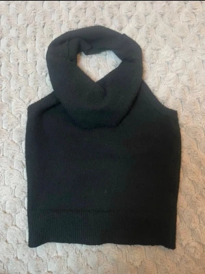 Svart stickad kragväst - Svart stickad kragväst med hög polokrage och ärmlös design. Perfekt att bära över en skjorta eller tröja för en trendig lager-på-lager-look. Mjuk och stretchig kvalitet som ger en snygg siluett.