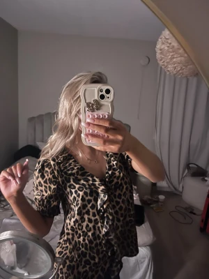 Leopardmönstrad blus med volang - Snygg blus med leopardmönster och volangdetalj framtill. Blusen har korta puffärmar och en v-ringad halsringning. Materialet ser ut att vara ett mjukt, lätt tyg som ger ett avslappnat men trendigt intryck. Perfekt för dig som vill sticka ut med ett djurmönster.