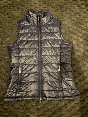 Mörkblå dunväst från Covalliero - Snygg mörkblå dunväst från Covalliero med hög krage och två dragkedjeförsedda fickor. Västen har quiltad design och glansigt material som ger en modern look. Perfekt för lager på lager och enkel att matcha till olika ridoutfits.