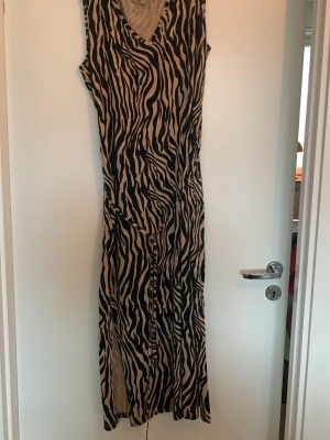 Zebramönstrad långklänning Flash Woman - Snygg långklänning från Flash Woman i zebramönster med svart och beige. Klänningen är ärmlös, har v-ringning och är gjord i mjuk ekologisk bomull. Perfekt för dig som vill sticka ut med ett djurinspirerat print.