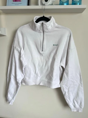 Vit cropped sweatshirt med dragkedja från Bikbok, stl S - Säljer en vit cropped sweatshirt från Bikbok med halv dragkedja framtill och hög krage (ca 6-7cm). Litet tryck i grönt på bröstet och är i bomull. Fått en gul missfärgning på framsidan (om man kollar noga), se bilder!
