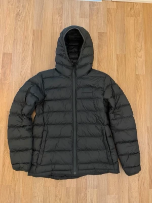 Grön dunjacka Peak Performance XL - Säljer en dunjacka från Peak Performance i storlek XL. Jackan har huva, dragkedja framtill och två sidofickor samt en innerficka. Klassisk quiltad design med diskret logga på bröstet. Perfekt för kalla vinterdagar/vår/höst och riktigt skön att bära. Aldrig använd bara tagit bort lapparna o säljer tyvärr för den blivit för stor. 