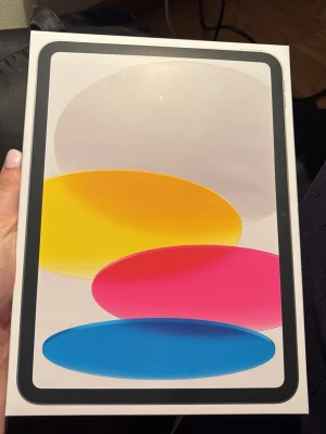 Apple iPad (A16) 128GB Wi-Fi - Säljer en Apple iPad (A16) 2025 med 128GB lagring och Wi-Fi. Surfplattan kommer i originalförpackning med färgglad framsida i vitt, gult, rosa och blått. Perfekt för surf, appar och streaming. Klassisk Apple-design i stilren vit kartong. Fick det som present men har aldrig öppnat den. 