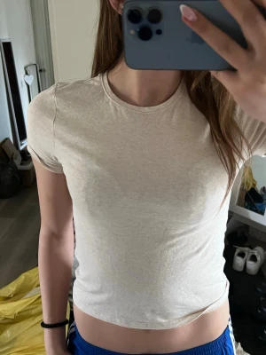 Beige basic t-shirt från H&M - En enkel och stilren beige t-shirt från H&M. T-shirten har rund halsringning och korta ärmar. Tillverkad i mjuk bomull som känns skön mot huden. Perfekt att matcha med jeans eller shorts för en clean look.
