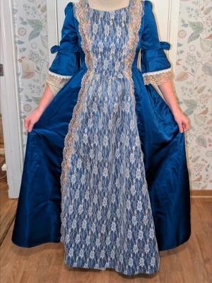 Vacker klänning  - Säljer en blå barockinspirerad klänning med spetsdetaljer framtill och på ärmarna, vackra band i ryggen. Klänningen har vida ärmar med spets. Perfekt till bal, cosplay eller maskerad med historiskt tema. Klänningen är endast provad.