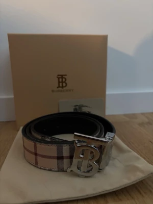 Burberry rutigt bälte med silverdetalj - Bältet är använt någon enstaka gång, säljer pga att jag inte använder det. Det finns ett lite slitage där man låser spännet syns på bilden, men inget som syns när du använder bältet annars är bältet felfritt snyggt för att sticka ut lite extra med din outfit. Om du har frågor kontakta mig.