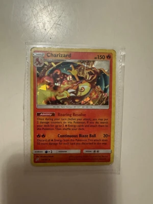 Charizard Pokémonkort holografiskt - Säljer ett holografiskt Charizard-kort från Pokémon TCG. Kortet har en eldig design med röd och gul färg, och är inplastat i ett skyddsfodral. Perfekt för samlare eller dig som vill boosta din lek med en ikonisk drake!