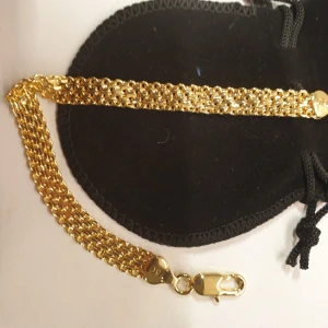 Guldfärgat kedjearmband 18K platerad - Armband i guldfärgad metall med tät, flätad kedjedesign och karbinlås. Märkt med 'ITALY' och '750', vilket indikerar 18 karat guld. Stilsäkert och elegant smycke som ger en lyxig känsla till din look.