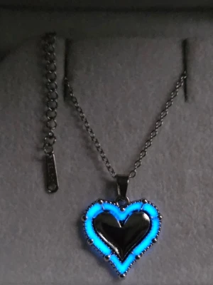 Halsband med hjärthänge i stål - Lyser blått!  - Snyggt handgjort halsband i rostfritt stål med ett hjärtformat hänge. Hänget har en unik design med dubbla hjärtan, där det yttre hjärtat är dekorerat med små pärlliknande detaljer och lyser blått i mörker efter att ha varit i vanligt dagsljus. Den lyser i flera timmar i mörker och både kedjan och hänget tål vatten, samt har en lång livslängd. Perfekt accessoar för att sticka ut.