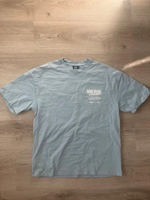 Ljusblå oversized t-shirt Black Squad - Säljer en ljusblå oversized t-shirt från Black Squad med tryck på bröstet. T-shirten har korta ärmar och är gjord i mjuk bomull. Perfekt för en chill och avslappnad stil. Storlek XS men är stor i storleken