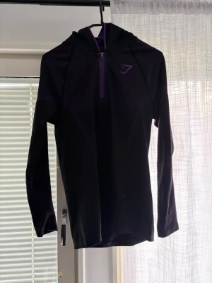 Svart hoodie från Gymshark - Säljer en svart långärmad hoodie från Gymshark med dragkedja framtill och diskret logga på bröstet. Tröjan har huva och är tillverkad i ett stretchigt funktionsmaterial som passar perfekt till träning.