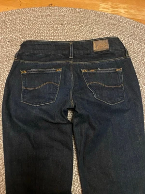 Mörkblå bootcut jeans från Lee - Midjan rakt över: 36cm. Innerben:76cm