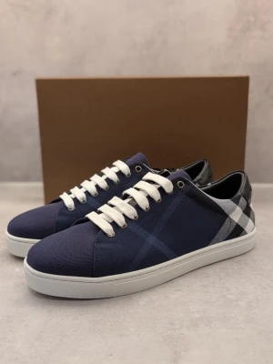 Blå rutiga sneakers från Burberry - Snygga sneakers från Burberry i marinblå textil med klassiskt rutmönster i blått, vitt och svart. Skorna har vita snören, vit sula och diskret Burberry-logga under sulan. Perfekt för dig som gillar stilrena och trendiga detaljer.