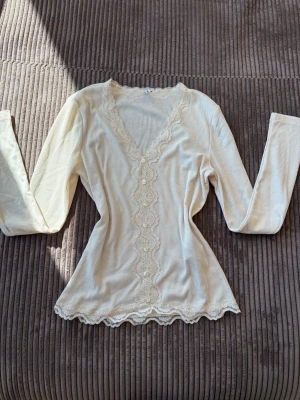 Vit ribbad topp med spetsdetaljer från ONLY - Supersöt vit ribbad topp med lång ärm och v-ringning. Toppen har fina spetsdetaljer längs halsringningen och framtill, samt vågig spetskant nedtill. Storleken är S,skickar inom 1-2dagar.Har aldrig använt!