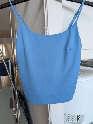 Blått linne från BikBok - Snyggt blått linne från BikBok i storlek XS. Toppen har tunna justerbara axelband och är tillverkad i ett mjukt, stretchigt material som sitter bekvämt mot kroppen. Perfekt för varma dagar eller som layering-piece. Kort modell.