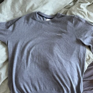 Grå GANT stickad tröja med rund hals - Den är använd en gång och jag kan inte ha den pågrund av att den är för liten, jag är 187 och den för för kort för mig men de här är en stilren grå stickad tröja med rund halsringning och diskret broderad logga på bröstet. Tröjan har långa ärmar och ribbade muddar vid ärmslut och nederkant. Perfekt för lager på lager och enkel att matcha med olika outfits. Det är storlek L men skulle rekommendera den här för folk som har M eller är runt 180 lång
