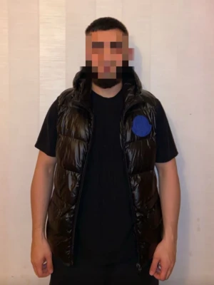 Svart dunväst från Moncler - Snygg svart dunväst från Moncler med glansig finish och hög krage. Västen har en blå patch med Moncler-logga på bröstet och dragkedja framtill. Perfekt att bära över en hoodie eller t-shirt för en trendig look.