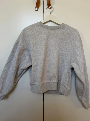 Grå basic sweatshirt - Enkel och stilren grå sweatshirt i mjukt material. Tröjan har rund halsringning, ribbade muddar vid ärmslut och nederkant samt en avslappnad passform. Perfekt att matcha med jeans eller mjukisbyxor för en chill look. Passar xs