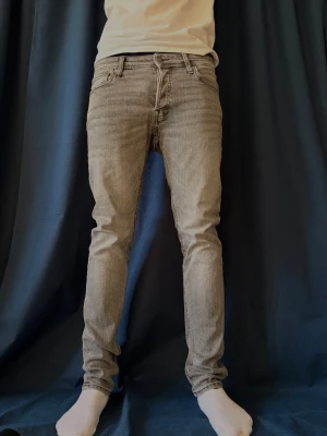 Grå slim fit jeans från jack and jones - Säljer ett par gråa slim fit jeans från jack and jones med klassisk femficksdesign och dragkedjegylf. Jeansen har en snygg tvättad look och raka ben. Perfekta för dig som gillar en stilren och modern vibe.