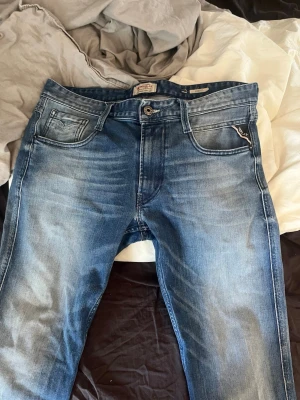 Blåa Replay jeans med tvättad look - Säljer ett par blåa jeans från Replay med snyggt tvättad finish och klassisk femficksmodell. Jeansen har raka ben och snygga små detaljer. Dessa är i storlek W31/L30, hör av er för frågor.