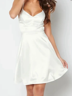 Vit kort klänning med spetsdetaljer - ⚠️endast använd två gånger ⚠️Snygg vit kort klänning i satinliknande material med smala axelband och v-ringning. Baksidan har vackra spetsdetaljer och knappar. Perfekt för sommarens alla tillfällen. 