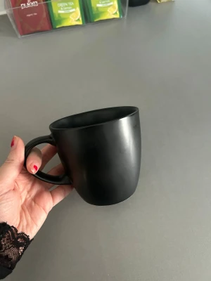 Svart matt mugg i keramik - Stilren svart mugg med matt finish och rundad form. Tillverkad i keramik och har ett bekvämt handtag som gör den enkel att hålla i. Perfekt för te, kaffe eller varm choklad. Enkel design som passar i alla kök.