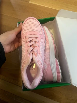 Rosa mesh sneakers med vita detaljer - Snygga rosa sneakers med vita detaljer och mesh-ovandel som ger bra ventilation. Skorna har klassisk snörning och en vit sula med rosa inslag. Perfekta för dig som gillar sportig och fräsch stil. Storlek 36 enligt. Aldrig använt 