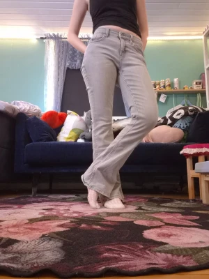 Ljusgrå bootcut jeans - Säljer ett par ljusgrå bootcut jeans med hög midja och klassiska fem fickor. Jeansen har en snygg utsvängd passform och är perfekta för dig som gillar en retrostil. Materialet är denim med tydliga sömmar.