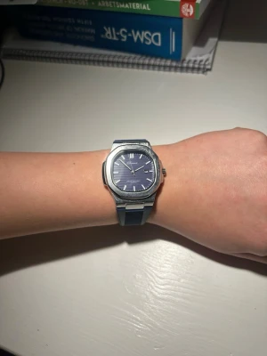 Blå klocka med blått silikonband - Snygg klocka med blå urtavla och matchande blått silikonband. Boetten är i silverfärgad metall och har en modern, fyrkantig form. Urtavlan har tydliga markeringar och visare, vilket gör den enkel att läsa av. Perfekt accessoar för dig som gillar stilrena detaljer.