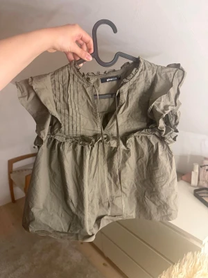 Olivgrön blus med volanger från Gina Tricot - Supersöt olivgrön blus från Gina Tricot med volangdetaljer vid axlarna och rynkade sömmar. Perfekt till sommaren/våren💚🥰