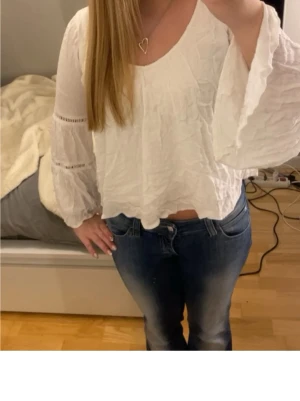 Vit blus med vida ärmar - Säljer en vit blus med v-ringning och vida, långärmade ärmar. Blusen har ett krinklat tyg och dekorativa spetsdetaljer på ärmarna. Perfekt till jeans för en avslappnad men trendig look.