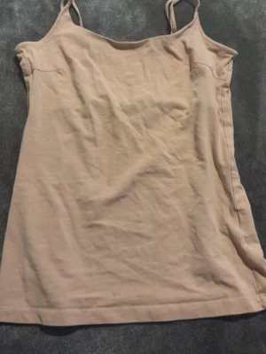 Beige linnetopp med smala axelband - Snygg beige linnetopp med smala axelband och enkel design. Toppen är ärmlös och har en rak passform som passar perfekt till både jeans och kjol. Tillverkad i mjukt bomullsmaterial för en bekväm känsla.