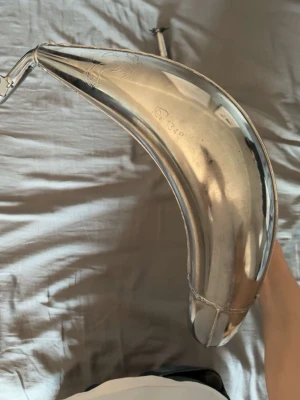 Voca chromed 50/70 - Säljer en kromad avgaskrök till moped eller cross. Den har en böjd, rundad form och är tillverkad i metall med blank finish. Perfekt för dig som vill uppgradera eller byta ut din nuvarande avgaskrök.